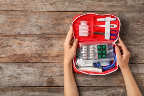 Mains ouvrant une trousse de premiers soins rouge remplie de matériel médical de base