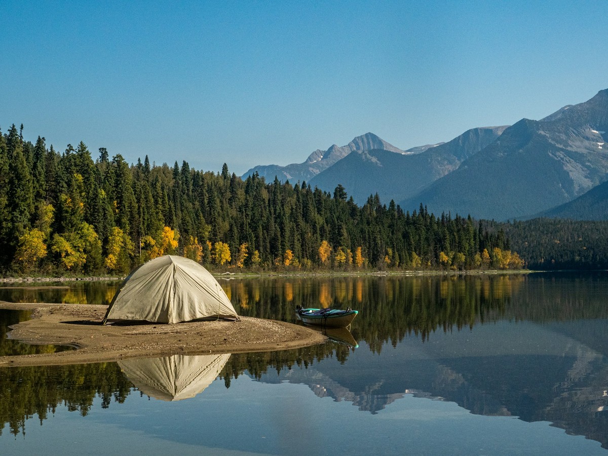 Tente de camping installée sur la rive d'un lac entouré de montagnes