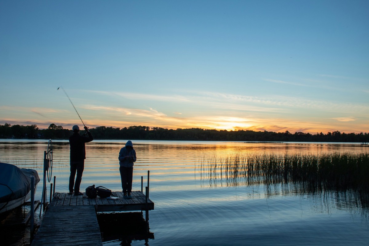Personne pêchant depuis le bord d'un lac calme au lever du soleil